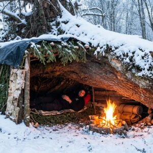 Solo winter bushcraft shelter built in deep snow for overnight survival